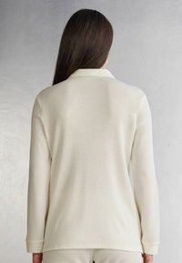 Crème-kleurige langesleeve top van textuurstof met een geribbeld patroon, voorzien van een klassieke kraag en een ontspannen pasvorm.