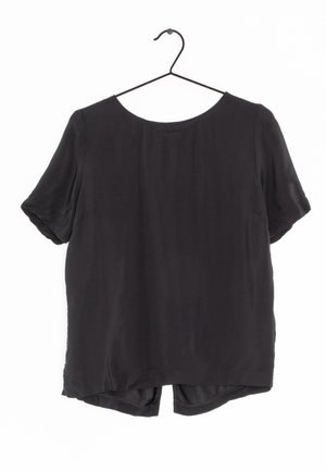 Top nero a maniche corte con scollatura tonda e orlo posteriore leggermente più lungo. Tessuto liscio e leggero. Appeso a un gancio nero.