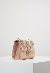 Borsa a tracolla beige in pizzo con motivo floreale, decorata con perle finte e gemme sulla patta, caratterizzata da una chiusura metallica e un design strutturato.