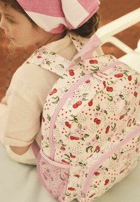 Fehér hátizsák cseresznye és virágmintával, rózsaszín kiegészítőkkel és hálós oldalzsebbel. Két cipzárral és párnázott pántokkal rendelkezik.