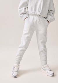Survêtement gris clair avec des poignets et une taille élastiques, doté de poches. Assorti avec des baskets métalliques argentées et des lacets blancs.