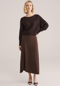 Pull en maille côtelée marron avec un col large, associé à une jupe marron fluide jusqu'au mollet. Texture lisse, détails minimalistes et coupe décontractée.