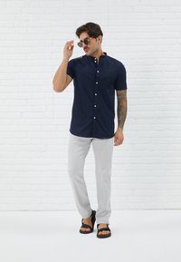 Short-sleeve, navy button-up shirt with a chest pocket, paired with light gray trousers and black sandals. Hypoallergenic fabric, smooth texture.