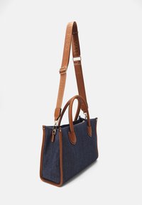 Denimväska med bruna läderdetaljer och handtag. Har en avtagbar rem och guldfärgad hårdvara. Strukturerad design med kontrasterande sömmar.