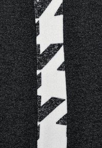 Närbild av svart och vit stickad tyg med djärva vita zick-zackmönster på en svart bakgrund.