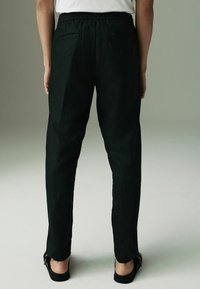 Pantaloni negri dintr-un material texturat, cu talie elastică și design drept, dotati cu buzunare la spate. Purtați cu sandale plate.