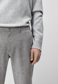 Pullover grigio a maglia abbinato a pantaloni grigi e neri a quadri con chiusura a bottone e tessuto testurizzato.