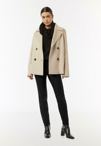 Beżowy płaszcz dwurzędowy z dużymi czarnymi guzikami, czarny golf, czarne wąskie spodnie i czarne botki na obcasie. Gładkie tekstury.