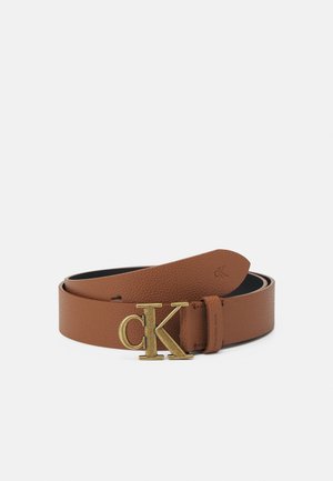 Brunt læderbælte rullet sammen med guld "cK" spænde og subtil præget branding på remmens ende, vist på en ensfarvet baggrund.