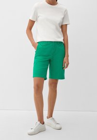 Shorts en coton vert avec une coupe décontractée, poches latérales et une ceinture classique, assortis à un t-shirt blanc uni et des baskets blanches.