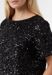 Czarny top pokryty błyszczącymi cekinami z okrągłym dekoltem i krótkimi rękawami, o gładkiej fakturze i misternych zdobieniach.