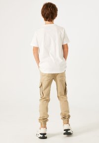 Witte katoenen t-shirt met korte mouwen, gecombineerd met beige cargobroeken met zijzakken en elastische boorden. Schoeisel: zwart-witte sneakers.