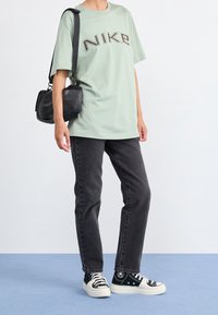 Ljusgrön bomullströja med "NIKE"-logotyp, tillsammans med svarta jeans och svart/vita sneakers. En liten svart axelväska kompletterar outfiten.