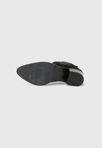 Black high-heeled shoe viewed from the bottom, showcasing a smooth outsole with subtle texture and a reinforced heel.