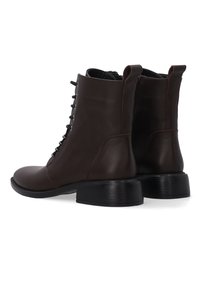 Para ciemno brązowych skórzanych botków za kostkę z sznurowaniem z przodu i czarnymi masywnymi niskimi obcasami, pokazanych z tyłu pod kątem na białym tle.