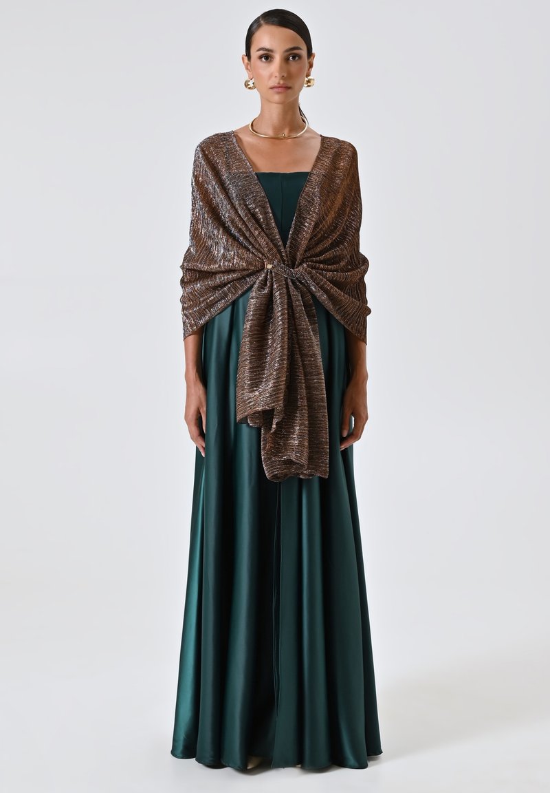 Un lungo abito in satin verde scuro abbinato a un scialle in bronzo metallico intrecciato, avvolto in vita, con una texture morbida e una drappeggiatura elegante.