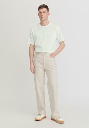 Lichtbeige rechte broekspijpen gecombineerd met een wit T-shirt met korte mouwen. De schoenen zijn crème-kleurig met beige accenten en veters.