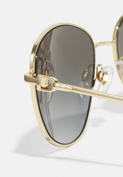 Ochelari de soare din metal aurit cu lentile gri închise, având o formă rotundă, un design cu ramă subțire și tampoane moi pentru confort.