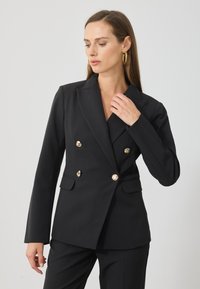 Μαύρο σακάκι διπλής όψης με αυλακωτά πέτα, κουμπιά χρυσού τόνου, μπροστινές τσέπες και εφαρμοστό σχέδιο. Λείο ύφασμα με δομημένο σχέδιο.