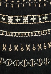 Black fabric featuring intricate cream and beige embroidery. Patterns include crosses, loops, and various geometric shapes.