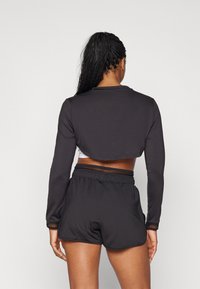 Schwarzes, kurzes Langarmoberteil und hochgeschnittene Shorts mit atmungsaktiven Mesh-Elementen; taillierte Passform, glatte Textur und elastischer Bund.