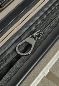 Primo piano di una zip nera con un tirante in metallo argento su un tessuto texture e superfici in plastica beige e nere adiacenti.