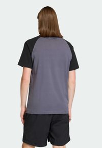 Tričko s krátkym rukávom so sivým telom a čiernymi raglánovými rukávmi. Tkanina pôsobí hladko a má voľný strih. Nosené s čiernymi šortkami.