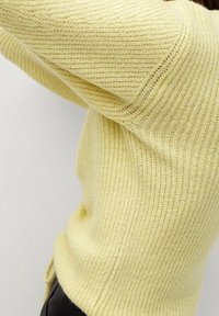 Pull tricoté texturé jaune avec un design côtelé et des manches longues, présentant une coupe décontractée et un tissu doux et subtil.