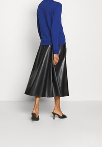 Modrý svetr s žebrovanými manžetami v kombinaci s dlouhou černou sukní z umělé kůže s předním švem a černými sandály s otevřenou špičkou.