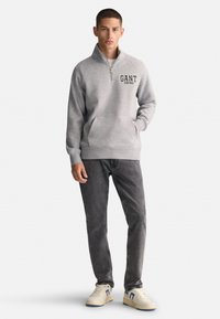 Szary polarowy sweatshirt z kołnierzem na ćwierć zamka, ozdobiony haftem "GANT" w kolorze czarnym. W zestawie z ciemnoszarymi dżinsami i białymi trampkami.