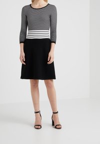 Robe rayée avec des manches trois-quarts, couleurs noir et blanc. Haut ajusté et jupe évasée texturée noire. Sandales à talons noires.