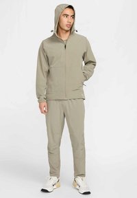 Lichtgewicht sportoutfit in beige met een capuchonjack met ritssluiting en bijpassende broek. Voorzien van elastische manchetten en zijzakken. Sneakers met zwarte details.