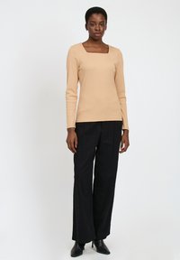 Top beige de manga larga con escote cuadrado combinado con pantalones de pierna ancha negros. Textura suave, diseño minimalista y silueta ajustada.
