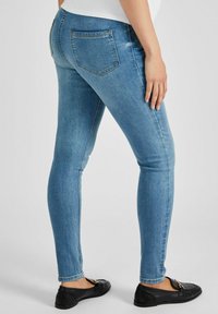 Gai ziliņi skinny džinsi, kas izgatavoti no denima, ar gludu tekstūru, standarta piecu kabatu dizainu un augstu jostasvietu. Redzami melni slip-on apavi.