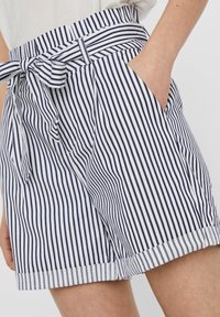 Raidalliset shortsit, joissa valkoinen ja laivastonsininen kuvio, solmittava vyötärönauha, sivutaskut ja käännetyt lahkeet. Puuvillakangas, sileä pinta.