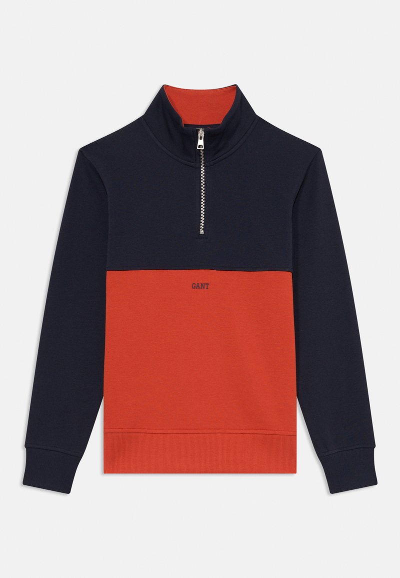 Felpa con zip a metà che presenta una parte superiore blu navy e una parte inferiore rossa brillante. Realizzata in tessuto morbido con polsini e colletto a coste, decorata con un logo.