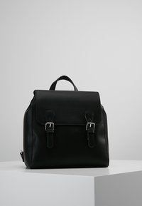 Mochila de cuero negro con cierre de solapa, dos hebillas metálicas, un asa superior y correas de hombro ajustables. Textura suave sin patrones.