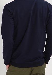 Marinblå crewneck sweatshirt med långa ärmar; tillverkad av mjukt och slätt material med ribbad nederkant och ärmslut. Enkelt, klassiskt design.