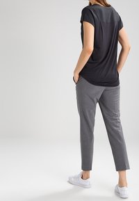 Haut noir à manches courtes avec un dos contrastant gris, associé à un pantalon gris fuselé et des baskets blanches ; tissu lisse et design décontracté.