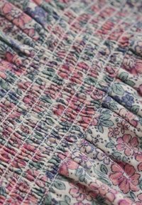 Bloemstoffen met een verzamelde textuur en roze, blauwe en groene bloemen op een witte achtergrond, met ingewikkelde stikpatronen.