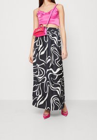 Růžový saténový crop top, černá maxi sukně s bílým vlnitým vzorem, růžová kabelka a růžové špičaté lodičky s akcenty ve tvaru srdce.