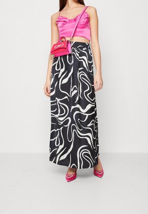 Top corto in raso rosa, gonna maxi nera con motivo ondulato bianco, borsa rosa e tacchi a punta rosa con dettagli a forma di cuore.