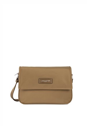 Sac en matériau synthétique tan avec une fermeture à rabat, présentant une plaque de logo de marque en métal et une sangle ajustable.