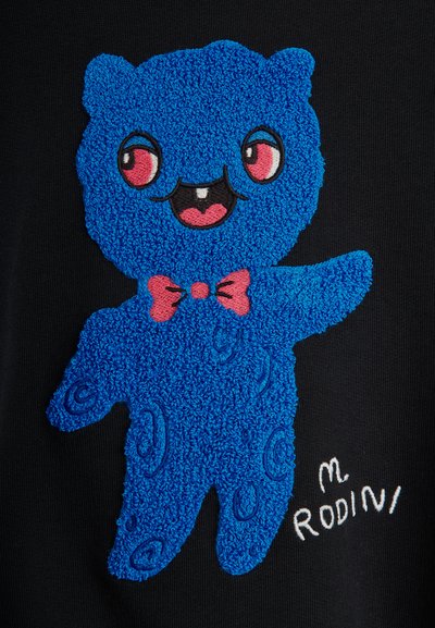 Μπλε αρκούδα με υφή, κόκκινα μάτια, κόκκινο παπιγιόν, χαμογελαστό στόμα με ένα δόντι, σηκωμένο χέρι, σε μαύρο φόντο με το κείμενο "M Rodini".