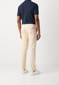 Lichtbeige broek met een rechte snit, gemaakt van katoen, met achterzakken en een klein label. Gecombineerd met een marineblauw polo en witte sneakers.