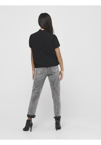 Blouse noire à manches courtes avec motif texturé, associée à un jean gris délavé et des bottines noires à talons hauts, vue de dos.