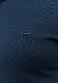 Granatowa koszulka polo o teksturowanym splocie; posiada haftowane małe logo zwierzęcia na lewej stronie klatki piersiowej.