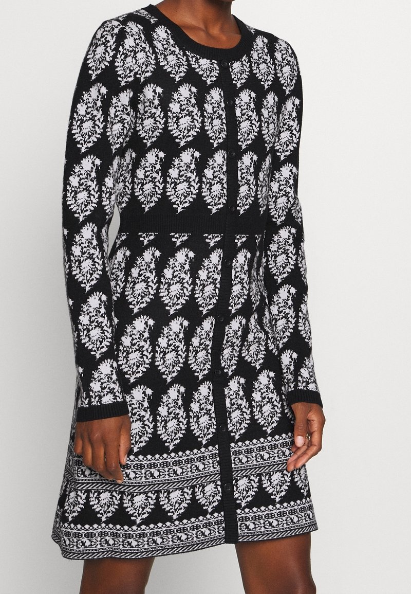 Robe en tricot noir et blanc avec motif de feuilles, manches longues, encolure ronde, fermeture par boutons et détails texturés à la taille et à l'ourlet.