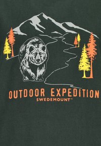 Ciemnozielona koszulka z grafiką niedźwiedzia, gór i drzew w odcieniach pomarańczowym i żółtym, z napisem "WYPRAWA NA ŚWIEDMOUNT".