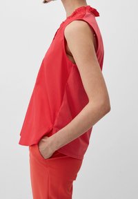 Top sin mangas color coral con un escote con volantes, que presenta un corte holgado y una textura suave, combinado con pantalones coral a juego.